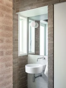 Modern bathroom with white sink and towel, white tiled floor, and concrete wall with small window