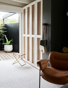 A mid-century modern lounge room featuring a brown leather armchair, white leather ottoman, and a white and brown basket in f