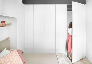 A minimalist bedroom with white paneling on the walls and a bed with a beige cushion and pink throw pillow.