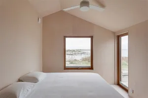 A minimalist bedroom with a window overlooking a coastal landscape.