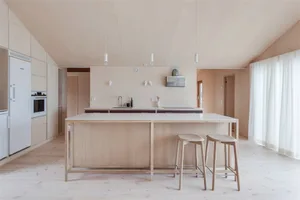 A minimalist residential kitchen featuring a wooden island and stools, surrounded by soft lighting and clean lines.