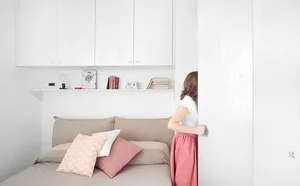 A minimalist bedroom with concrete walls, a bed, and colorful pillows.