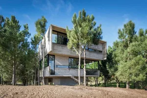 A modern, two-story house with concrete exterior surrounded by trees and sand