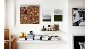 A modern minimalist living room with white walls, floating shelves, books, sculptures, and various artworks hanging on the wa