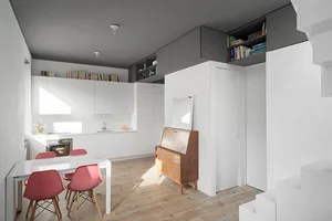 A minimalist modern kitchen with white cabinets, a glass dining table, and pink chairs.