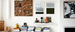 A modern living room featuring abstract artworks on the walls, a wooden floor, and a white shelf with books and decorative it