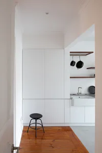 Modern minimalist kitchen featuring sleek white cabinetry, a wooden floor, and a black stool.