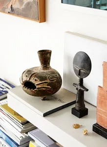 A ceramic vessel with a fish design on a stack of books, accompanied by a figurine and jewelry.