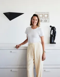 A woman dressed in white standing in front of a white counter with minimalist sculptures and artwork.