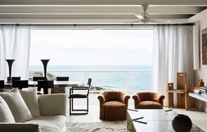 A minimalist living room with a large window overlooking the ocean, featuring fabric seating and modern furniture.