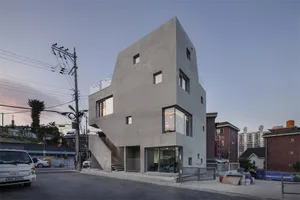 A minimalist, modern building with a concrete exterior. The structure has multiple floors with large windows and a unique sha
