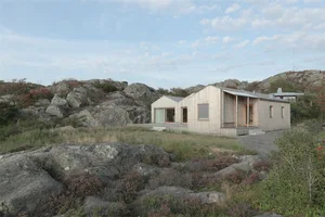 A modern residential architecture house with wood siding and large windows set against a rocky landscape.