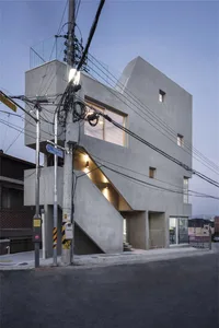 An exterior view of a modern commercial space featuring concrete architecture and illuminated interior elements.
