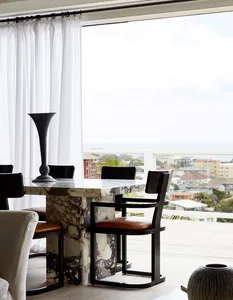 A modern dining room features a rectangular marble table with black metal chairs and a large window overlooking a cityscape.