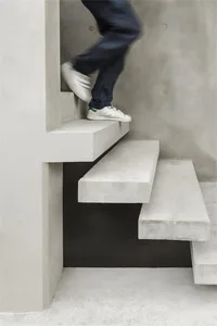A modern staircase constructed from white concrete with a person wearing white sneakers with green straps climbing it.