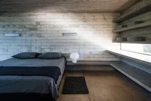Modern minimalist bedroom with concrete walls, floor, and shelves.