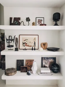 A well-curated display shelf featuring various sculptures, artworks, and objects arranged on three shelves, showcasing a dive