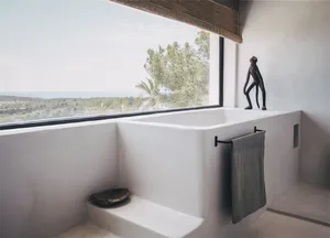Modern minimalist bathroom featuring a concrete bathtub and towel rack with a view of the ocean through a large window.