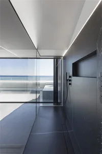 Modern minimalist bathroom with glass walls and marble finishes, featuring sleek design and ocean view.