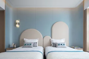 Modern minimalist bedroom with two white beds against blue walls, featuring curved headboards, white bedding, and light blue 
