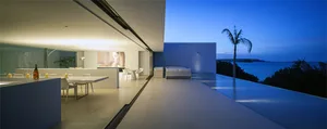 Modern minimalist residential interior with glass walls overlooking the ocean at dusk
