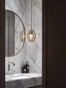 A sleek, modern bathroom with marble walls, a circular mirror, and a hanging crystal chandelier.