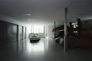Modern minimalist garage interior with concrete floors, white walls, and a white car parked inside.