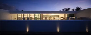 A modern residential exterior with a pool and interior lighting visible through large windows.