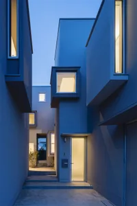 A modern residential exterior featuring concrete walls and large windows at dusk.