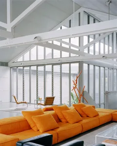 Modern living room with a vibrant orange sectional sofa, black and white chairs, and sleek furniture.