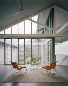 A minimalist living room with glass and metal furniture, large windows, and natural light.