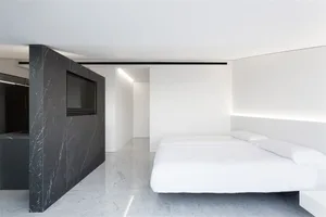 A minimalist bedroom with white walls, black marble accents, and two white beds.