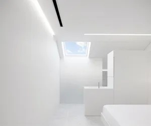 Modern, minimalist bedroom with white walls, ceiling, and floor. Features a large window with natural light.