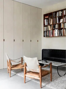 A modern living room with wooden chairs and a black sofa, featuring a bookshelf filled with books.