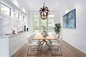 A modern dining room featuring white furniture and a marble backsplash with a geometric light fixture hanging above the table
