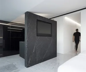 A modern kitchen with a black marble backsplash and black marble countertops, featuring a black television mounted on the wal