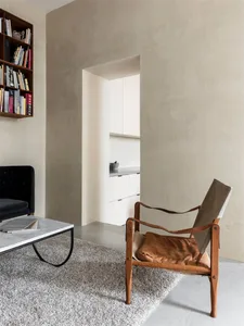 A minimalist living room with a modern design, featuring a concrete wall, a leather armchair, a marble coffee table, and a bo