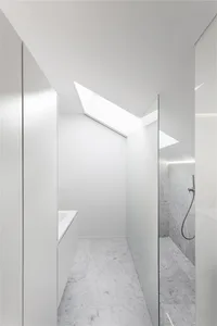 A minimalist bathroom with marble walls and floor, featuring a skylight and white fixtures.