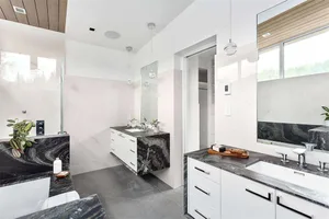 A modern bathroom with sleek marble countertops and flooring, featuring a minimalist design with white cabinetry and pendant 