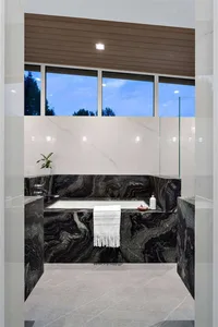 Modern bathroom featuring black marble with a white towel hanging on the edge of the bathtub and a plant on the left side.