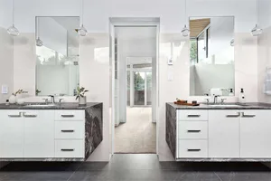 Modern bathroom with marble countertops, white cabinets, and large mirrors.
