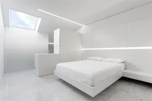 A modern white bedroom with a floating bed, white walls, and a white ceiling light.