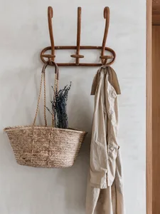 An entryway scene featuring wooden hooks, a woven basket filled with dried flowers, and a beige coat hanging on the hooks.