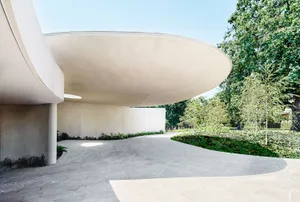 Modern architectural design featuring a sleek, concrete exterior with curved walls and a large, overhanging canopy.