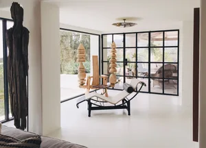 Modern living room with white furniture, large windows, and abstract sculptures
