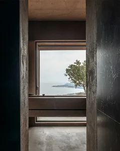 Industrial-style interior with concrete walls and large window overlooking a coastal landscape.