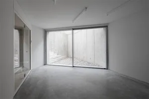A minimalist space with a concrete ground and wall, featuring a view of a gravel courtyard and steps leading downwards.