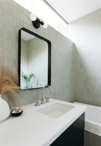 Modern, minimalist bathroom featuring green tiles, a white countertop, and a black-framed mirror.