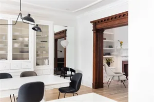 A modern white interior space featuring a white cabinet, black lighting, and wooden floor.