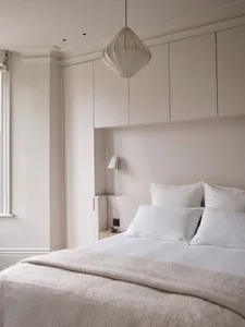A minimalist bedroom with muted tones and soft textures, featuring a bed with white bedding and a light-colored headboard, si